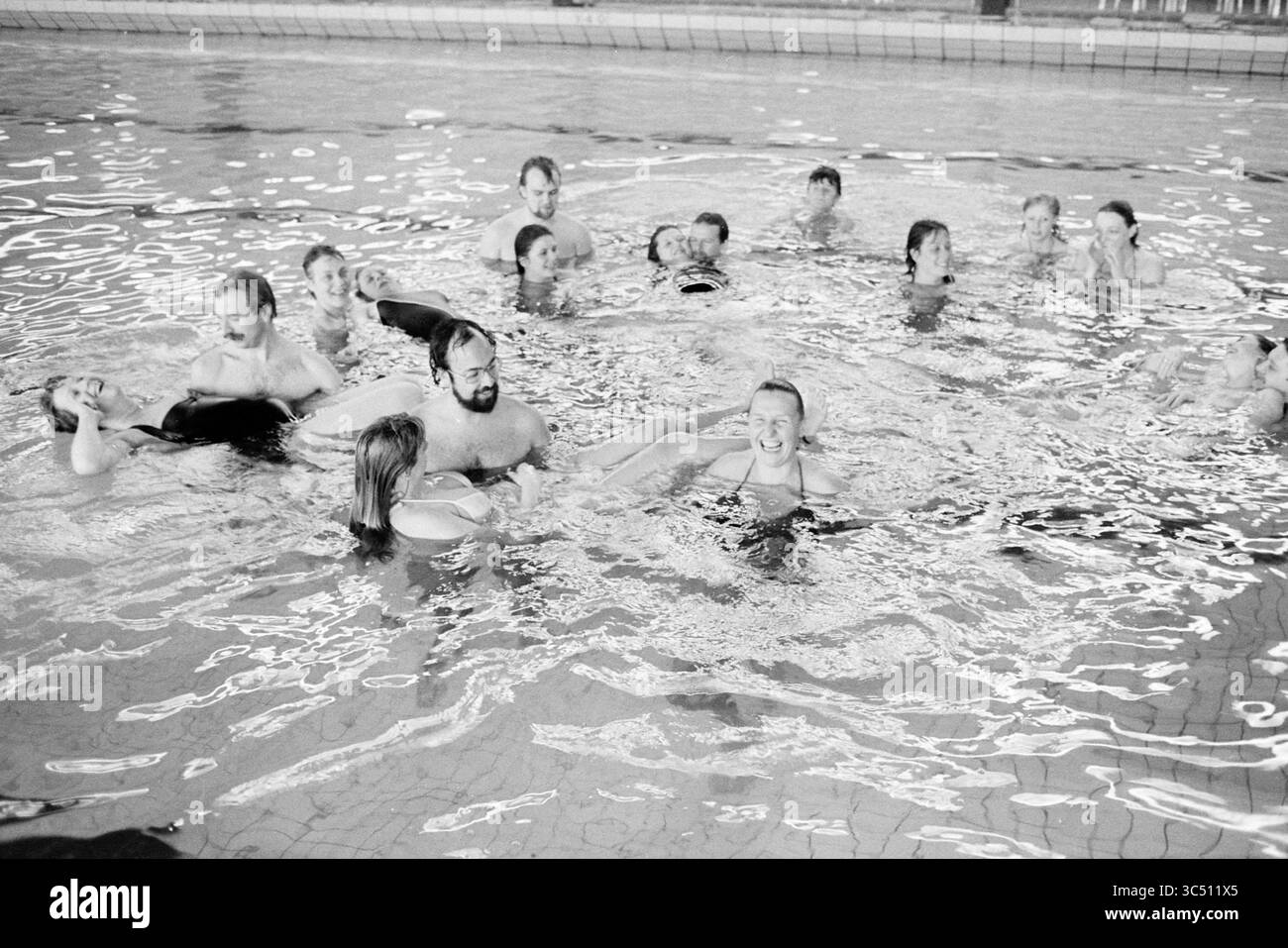 Le donne incinte nuotano con i loro mariti, 00-04-1984 Whizgle News, Dutch Desk, Paesi Bassi, 1950-2000 Un grande gruppo di persone si diverte in una piscina, con un po' d'acqua che spruzza e altre si rilassano o ridono. La scena trasmette un senso di divertimento e cameratismo tra i partecipanti. Foto Stock