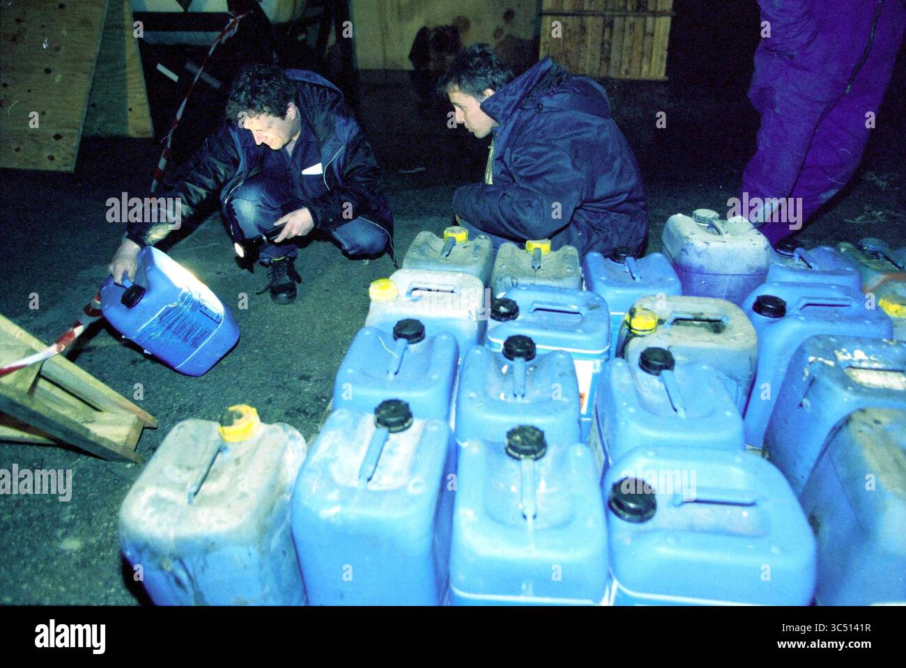 Polizia ambientale portuale, IJmuiden, IJmuiden, Paesi Bassi, 25-03-2003 Whizgle News, Dutch Desk, Paesi Bassi, 1950-2000 due persone esaminano i contenitori blu, utilizzando una torcia per ispezionarne il contenuto, mentre altri contenitori simili sono impilati nelle vicinanze. L'impostazione sembra essere un'area di lavoro, eventualmente associata a una ricerca o a un'indagine. Foto Stock