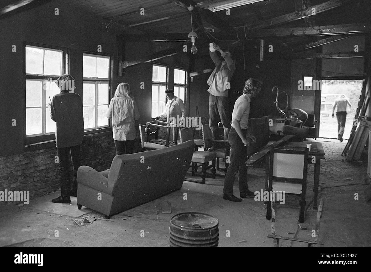 Work Sleep-in Zandvoort., Work, 15-06-1972 Whizgle News, Dutch Desk, Paesi Bassi, 1950-2000 Un gruppo di individui è impegnato in qualche forma di ristrutturazione o di lavori di costruzione all'interno di uno spazio rustico. Alcuni regolano l'illuminazione, mentre altri sono posizionati intorno alla stanza, sia in funzione che in funzione. L'ambiente suggerisce un mix di collaborazione e lavoro manuale, con strumenti e mobili sparsi in tutto il mondo. Foto Stock
