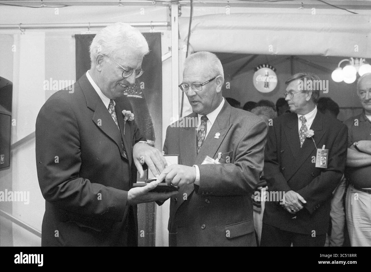 Coppetta Coca-Cola: R. Ravenstein riceve Medal of Merit, Haarlem, Paesi Bassi, 28-07-1997 Whizgle News, Dutch Desk, i Paesi Bassi, 1950-2000 due uomini in abbigliamento formale si impegnano in uno scambio cerimoniale, con uno che presenta una medaglia o un premio all'altro. Entrambi gli uomini mostrano espressioni di rispetto e apprezzamento. Sullo sfondo, un piccolo gruppo di spettatori osserva il momento, alcuni indossano distintivi. L'ambiente sembra essere un evento festivo o formale, indicato da decorazioni e illuminazione ambientale. Foto Stock