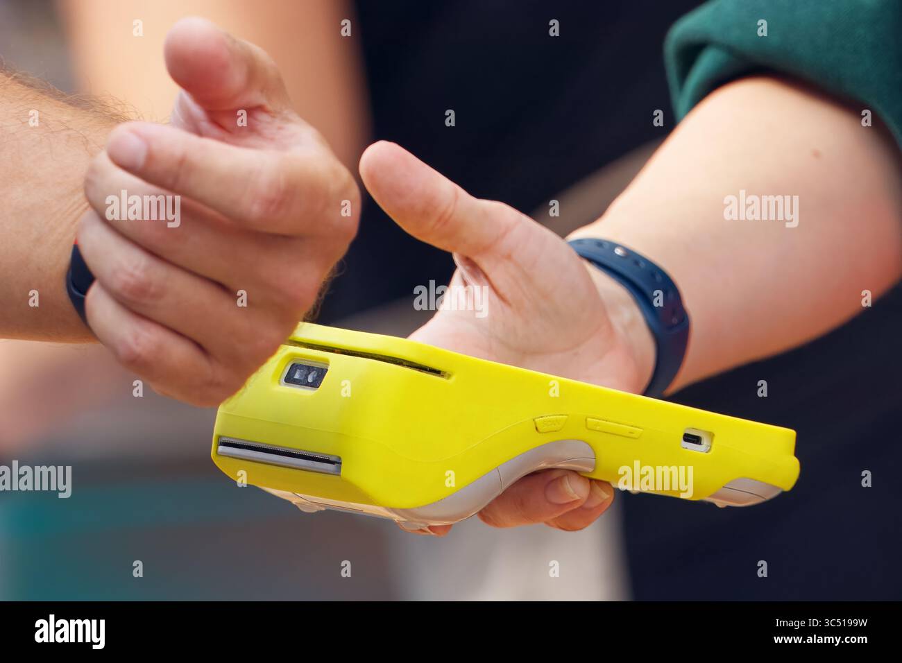 Un cliente che effettua un pagamento contactless utilizzando un dispositivo indossabile durante un evento all'aperto, pagando collegando uno smartwatch a un terminale di pagamento. L'i Foto Stock