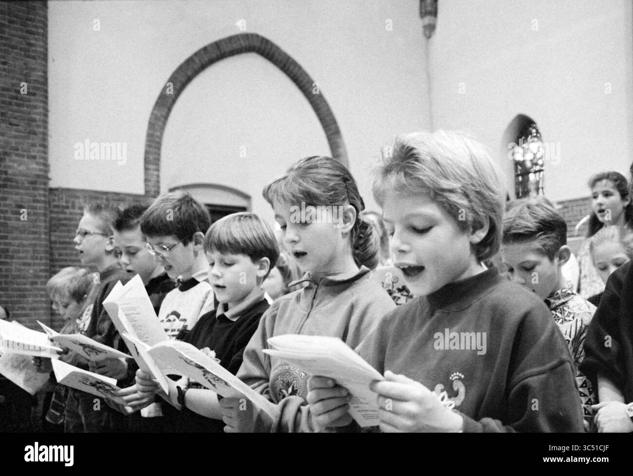 Choir, Haarlem, Paesi Bassi, 21-11-1992 Whizgle News, Dutch Desk, i Paesi Bassi, 1950-2000 Un gruppo di bambini si erge in un coro, cantando con entusiasmo mentre tengono spartiti musicali. Le loro espressioni trasmettono gioia e concentrazione, mentre l'architettura dello spazio aggiunge all'atmosfera delle performance. Foto Stock