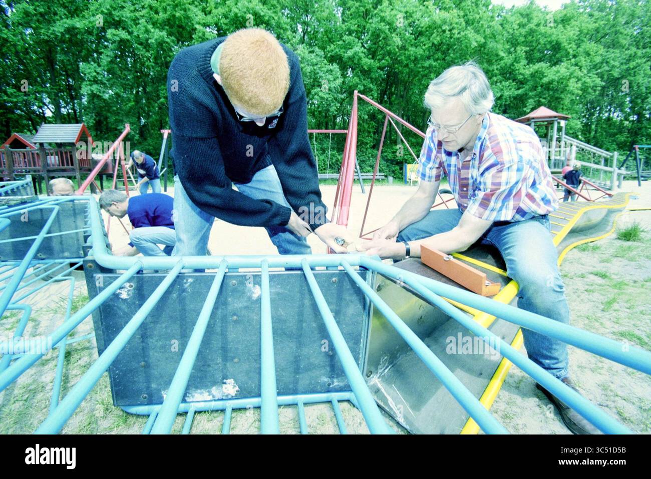 Parco giochi a Santpoort, Santpoort, 09-06-2001 Whizgle News, Dutch Desk, Paesi Bassi, 1950-2000 due persone stanno lavorando insieme per riparare le attrezzature del parco giochi, dimostrando il lavoro di squadra in mezzo a uno sfondo di colorate strutture del parco giochi. Altre persone possono essere viste in background, contribuendo al progetto. Foto Stock