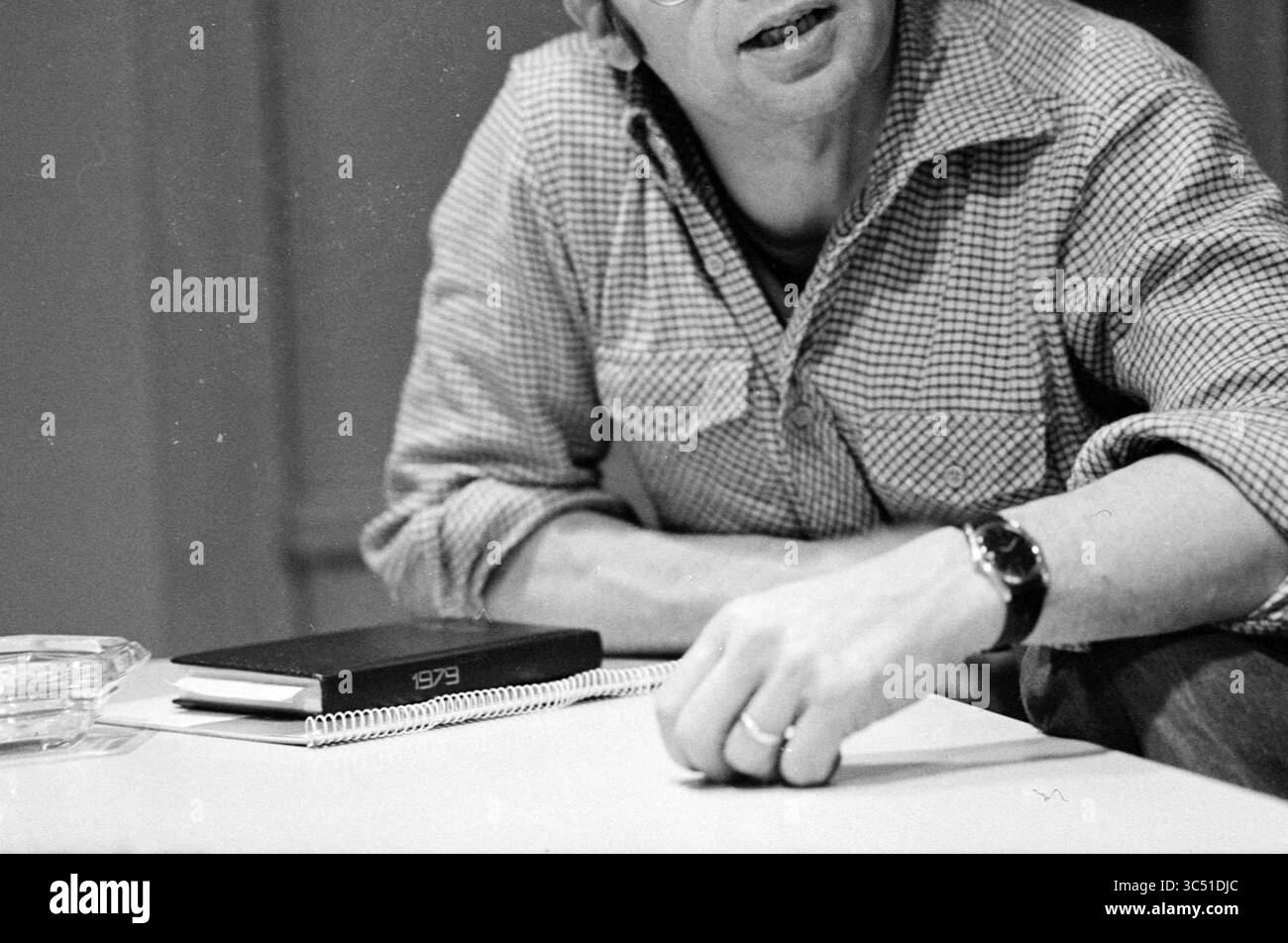 KRO radio Production Manager Gerard Hulshof, radio, 12-02-1979 Whizgle News, Dutch Desk, Paesi Bassi, 1950-2000 Una persona con una camicia a scacchi poggia la mano su un foglio di carta bianco, mentre un quaderno e un vaso si siedono sul tavolo vicino. La scena trasmette un senso di contemplazione e creatività. Foto Stock