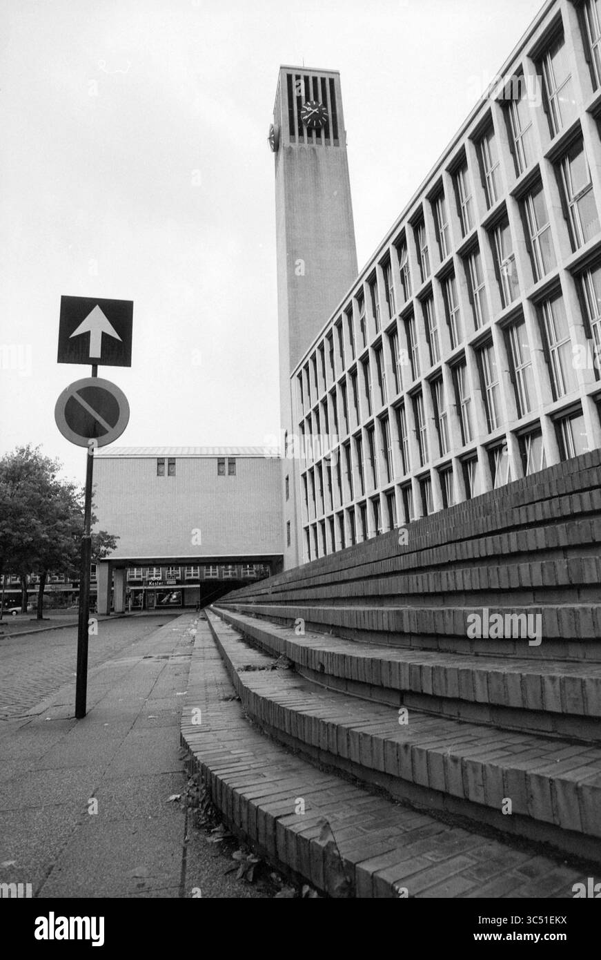 Esterno del municipio Velsen, Town Hall, Velsen, 25-08-1989 Whizgle News, Dutch Desk, i Paesi Bassi, 1950-2000 Un edificio moderno con una distintiva torre dell'orologio è incorniciato da ampi e graduali scalini che conducono all'ingresso. In primo piano, un segnale stradale indica una direzione a senso unico, mentre un segnale di divieto di ingresso aggiunge un contesto urbano. La scena generale trasmette un mix di stile architettonico e funzionalità. Foto Stock