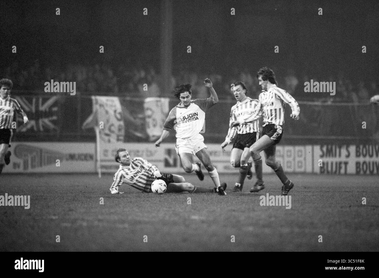 Partita di Coppa Telstar - Vlissingen, Telstar football, 03-02-1989 Whizgle News, Dutch Desk, Paesi Bassi, 1950-2000 Un giocatore con una maglia bianca evade abilmente un placcaggio scorrevole da un avversario, mentre altri due giocatori con maglie a strisce lo guardano, pronti a partecipare al gioco. La scena cattura l'intensità e la competitività di una partita di calcio. Foto Stock