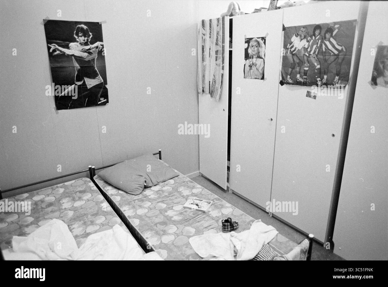 Camera da letto squallida ('Report on temporary living space Haarlem'), 21-06-1979 Whizgle News, Dutch Desk, Paesi Bassi, 1950-2000 Una piccola camera con due letti non fatti con lenzuola e cuscini increspati. Poster di varie figure adornano le pareti, mentre un armadio con porte chiuse si trova nell'angolo. L'atmosfera generale suggerisce uno spazio abitativo e informale. Foto Stock