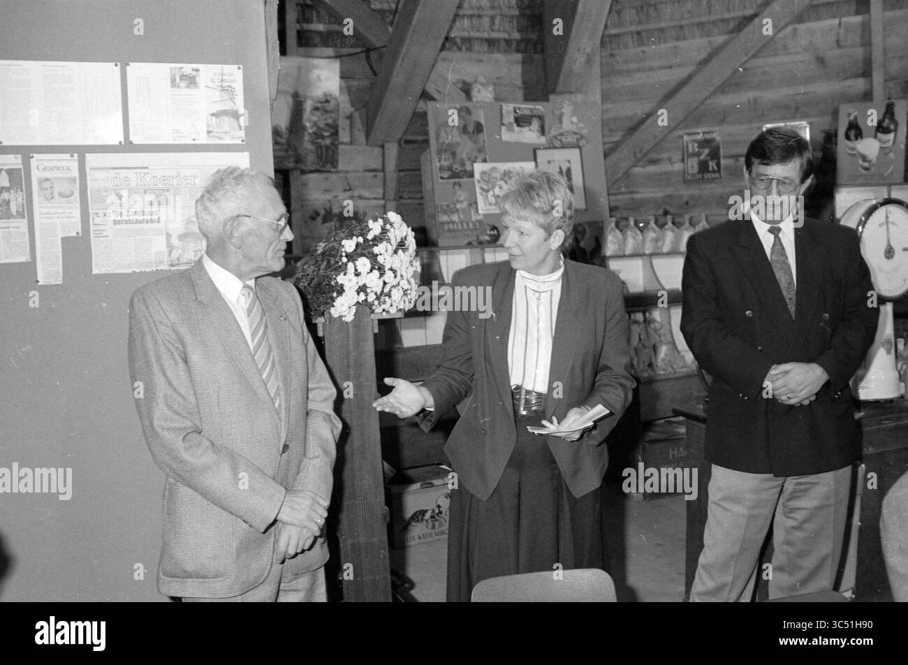 Consegna del assegno al mulino, Driehuis, Santpoort-Noord, Velserhooftlaan 17, 28-10-1991 Whizgle News, Dutch Desk, Paesi Bassi, 1950-2000 Un gruppo di tre persone si occupa di conversazione in un ambiente rustico, con una persona che gestisce in modo espressivo mentre altri ascoltano con attenzione. L'atmosfera suggerisce un momento di riconoscimento o celebrazione, possibilmente correlato a risultati o a un evento nella comunità, con poster e articoli visualizzati sullo sfondo. Foto Stock