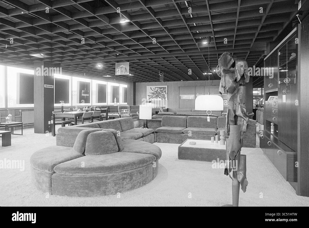 Interior Inden Furniture Beverwijk, negozi e chioschi, 04-04-1977 Whizgle News, Dutch Desk, Paesi Bassi, 1950-2000 Una moderna area lounge con un ampio divano circolare, un tavolino da caffè minimalista ed eleganti opere d'arte alle pareti. Il design aperto è completato da sculture uniche e da una struttura ben definita del soffitto, che crea un'atmosfera invitante ma sofisticata. Foto Stock