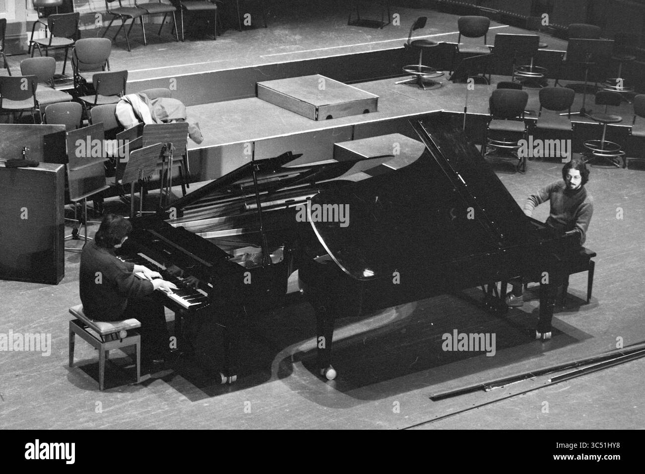 Van Kempen e Helledoorn, pianisti, musica, 21-01-1983 Whizgle News, Dutch Desk, i Paesi Bassi, 1950-2000 due pianisti si esibiscono fianco a fianco su pianoforti a coda, circondati da una sala da concerto vuota con sedie disposte sullo sfondo. L'atmosfera suggerisce una prova o preparazione per una performance, con spartiti musicali visibili sui loro stand. Foto Stock