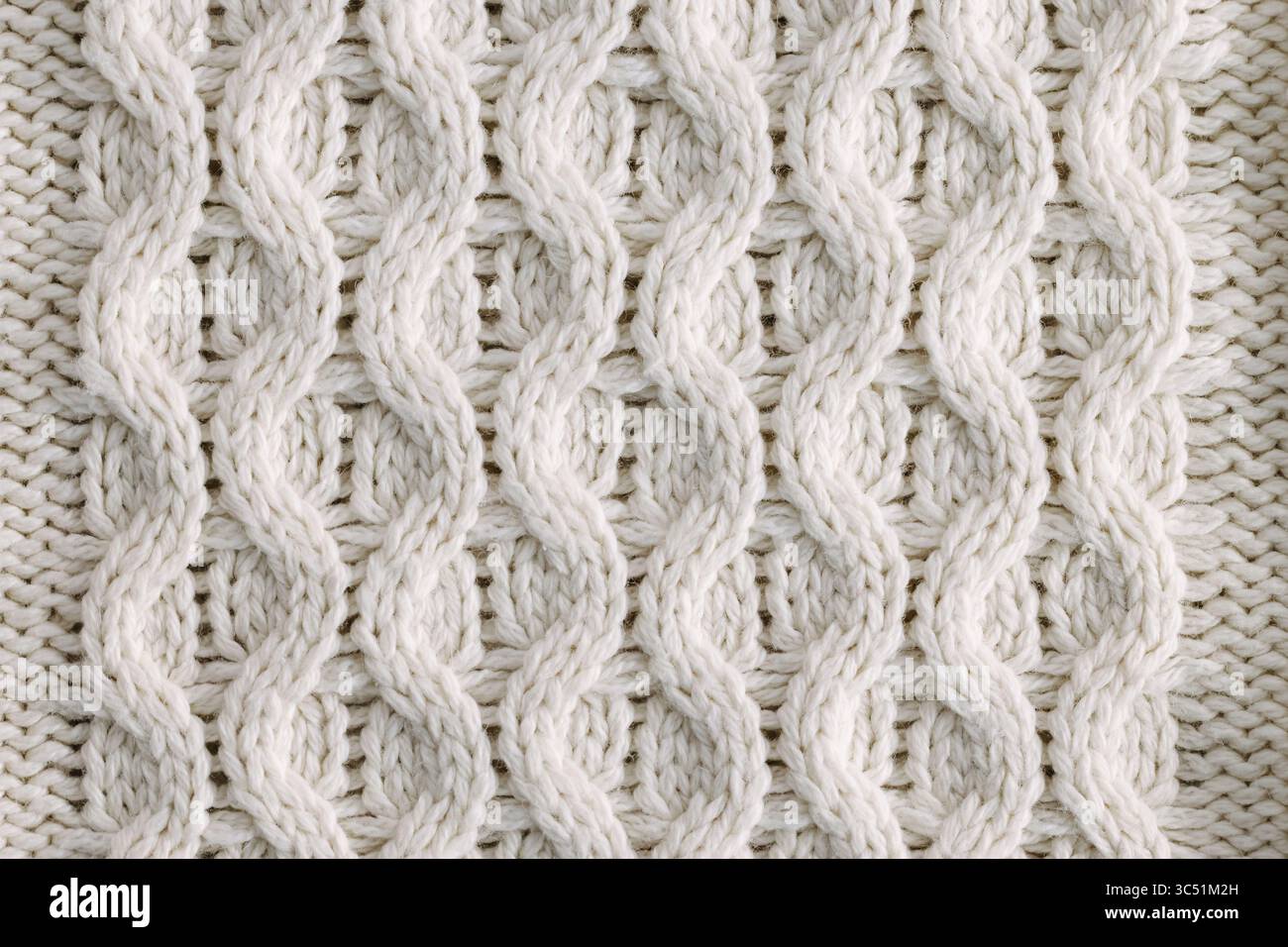 Un'immagine dettagliata in primo piano di un motivo bianco a maglia a cavo, che mette in risalto l'intricata texture e la maestria artigianale del tessuto tessuto. Foto Stock