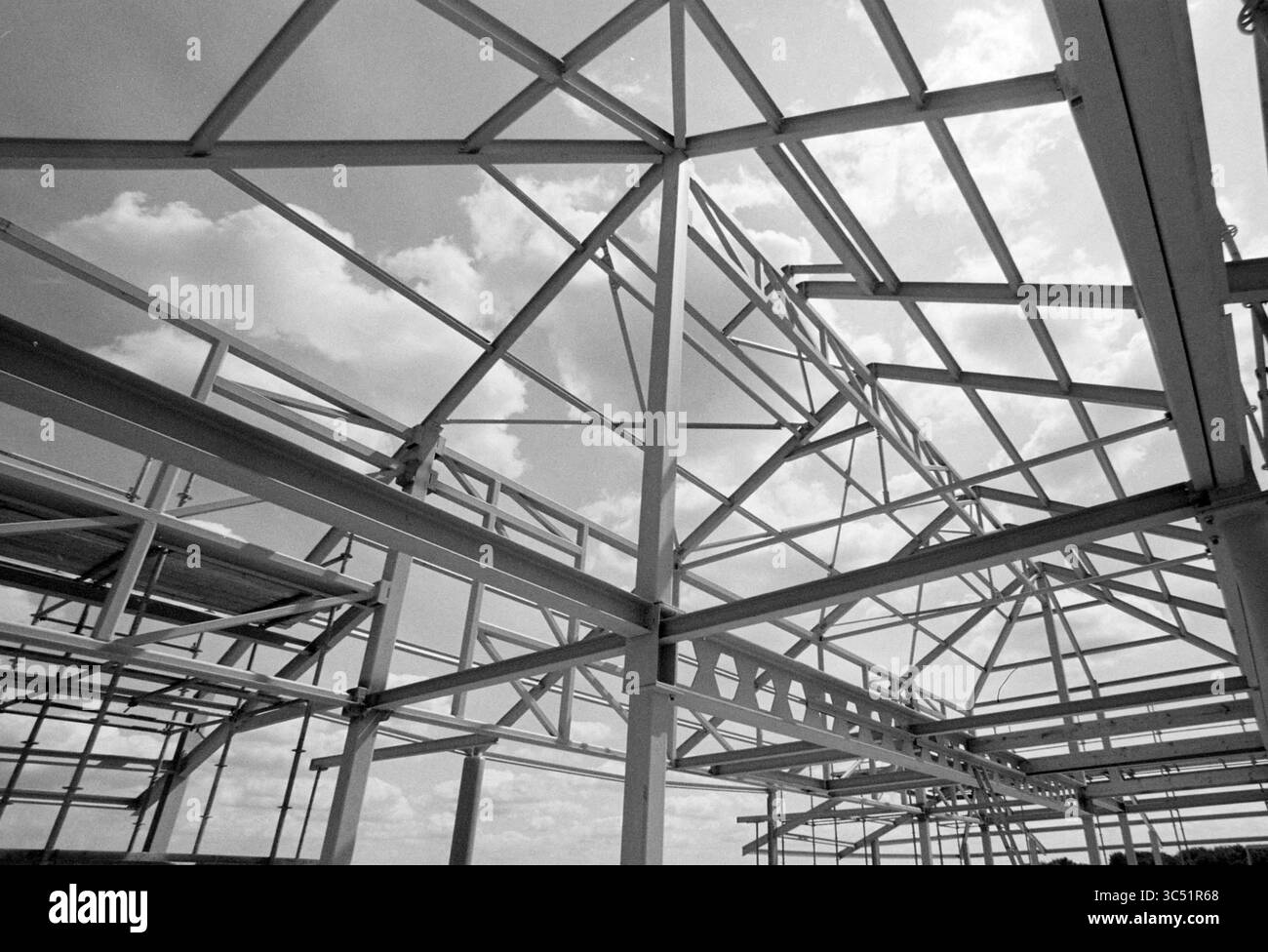 Struttura in acciaio di un capannone Whizgle News, Dutch Desk, Paesi Bassi, 1950-2000 struttura scheletrica di un edificio in costruzione, che rivela intricate travi in acciaio e un vasto cielo pieno di nuvole sopra. Foto Stock