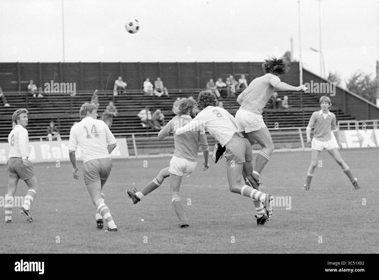 Partita di calcio, 00-00-1978 Whizgle News, Dutch Desk, Paesi Bassi, 1950-2000 Un momento dinamico sul campo di calcio mentre un giocatore salta in aria per dirigere la palla, mentre altri si impegnano in una partita intensa. I giocatori mostrano il loro spirito competitivo, con uno che tenta un calcio e altri pronti all'azione. Gli spettatori sullo sfondo mettono in risalto l'atmosfera vivace del gioco. Foto Stock