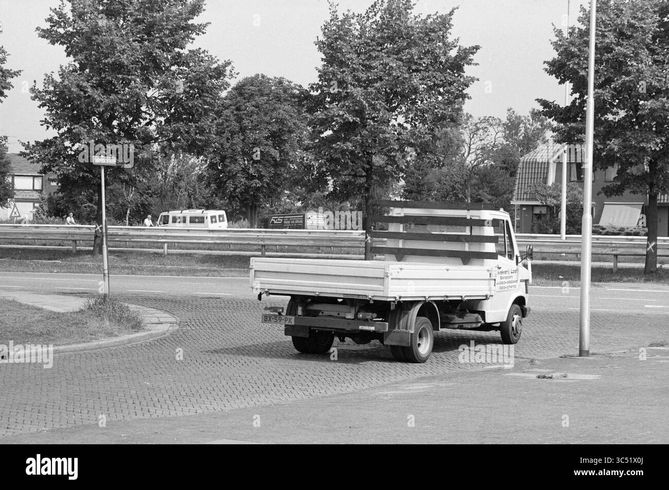 Incrocio Santpoortse Dreef, IJmuiden Highway, strade, costruzione di strade, semina di strade, Santpoort-Noord, Santpoortse Dreef, 08-08-1988 Whizgle News, Dutch Desk, Paesi Bassi, 1950-2000 Un piccolo autocarro a pianale attraversa una rotonda, circondata da alberi ed edifici residenziali sullo sfondo. La scena cattura un momento tranquillo in un'area suburbana, con il veicolo che sembra essere in transito. Foto Stock