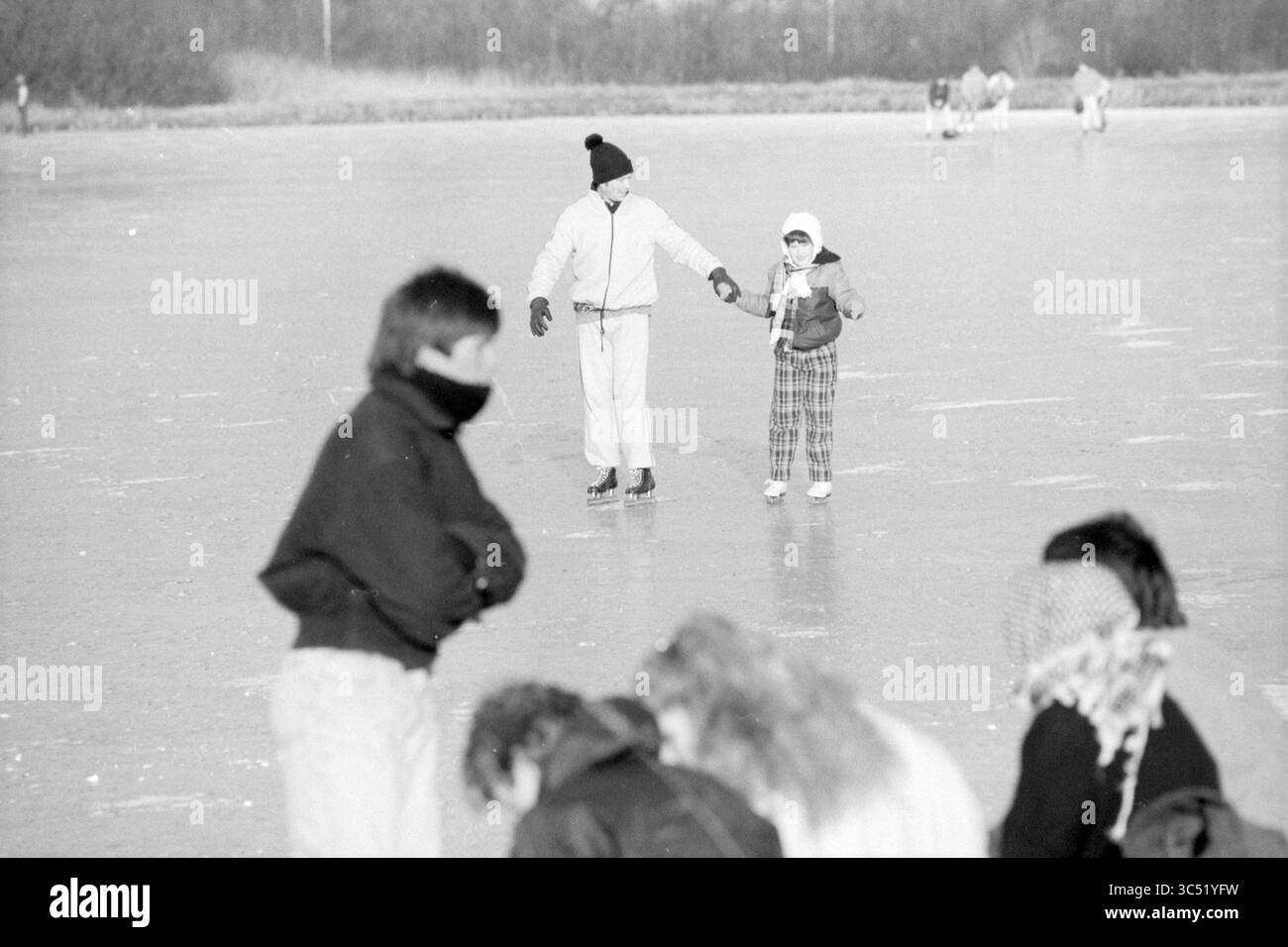 Divertimento di pattinaggio Whizgle News, Dutch Desk, Paesi Bassi, 1950-2000 bambini giocano e pattinano su una superficie ghiacciata, alcuni confezionati con abbigliamento invernale. In primo piano, un gruppo si inclina verso il basso, concentrandosi su qualcosa sul ghiaccio, mentre due bambini scivolano insieme sullo sfondo, mano nella mano, godendosi la giornata invernale. Foto Stock