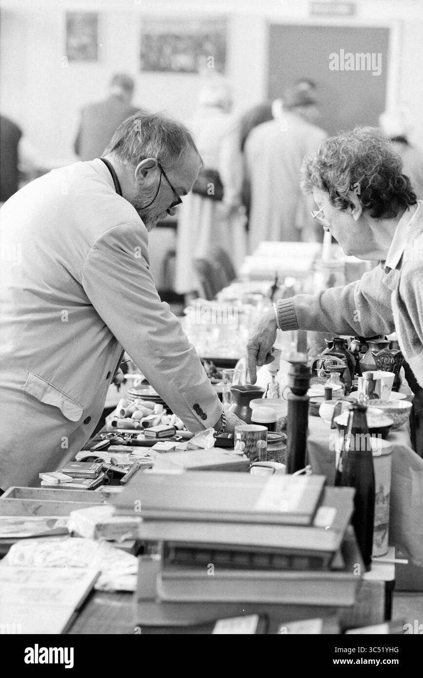 Collection Fair, Zandvoort, 09-05-1992 Whizgle News, Dutch Desk, Paesi Bassi, 1950-2000 due persone esaminano vari oggetti su un tavolo in un vivace mercato o fiera, circondato da una folla. L'ambientazione include un assortimento di oggetti da collezione, libri e curiosità, creando un'atmosfera di esplorazione e conversazione. Foto Stock