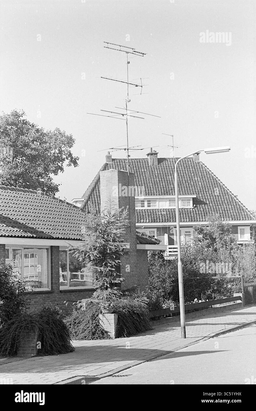 Antenna TV sul tetto, televisione, 19-09-1969 Whizgle News, Dutch Desk, Paesi Bassi, 1950-2000 Una tranquilla strada residenziale presenta affascinanti case con tetti spioventi e giardini ben tenuti. Le antenne si innalzano sopra i tetti, mentre nelle vicinanze si trova un lampione che crea un'atmosfera serena nel quartiere. Foto Stock