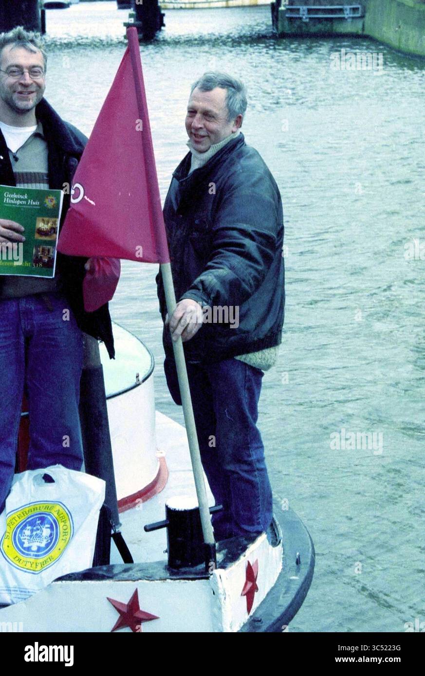 Boat St. Petersburg, Haarlem, Paesi Bassi, 14-01-2003 Whizgle News, Dutch Desk, i Paesi Bassi, 1950-2000 due persone sono in piedi su una barca, con una bandiera mentre l'altra mostra un libro. Lo sfondo presenta acqua, suggerendo un ambiente marittimo. Entrambi sembrano godersi il loro tempo all'aperto. Foto Stock
