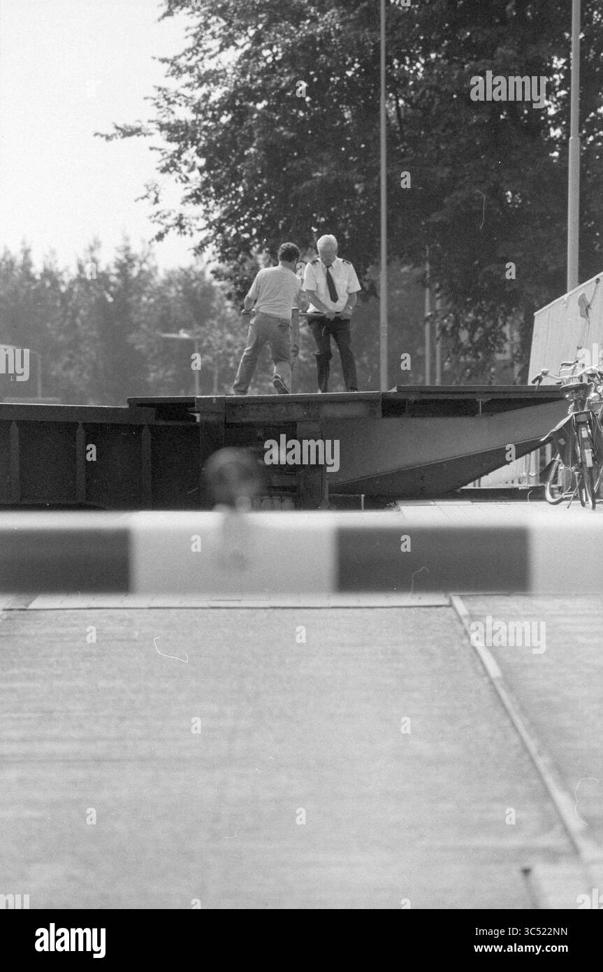 Defective Waarderbrug, Haarlem, Nederland, 26-07-1991 Whizgle News, Dutch Desk, i Paesi Bassi, 1950-2000 due persone sono in piedi su una piattaforma, impegnati in conversazione o attività, con una barriera visibile in primo piano. Le biciclette sono parcheggiate nelle vicinanze e gli alberi possono essere visti sullo sfondo, suggerendo un ambiente all'aperto. Foto Stock