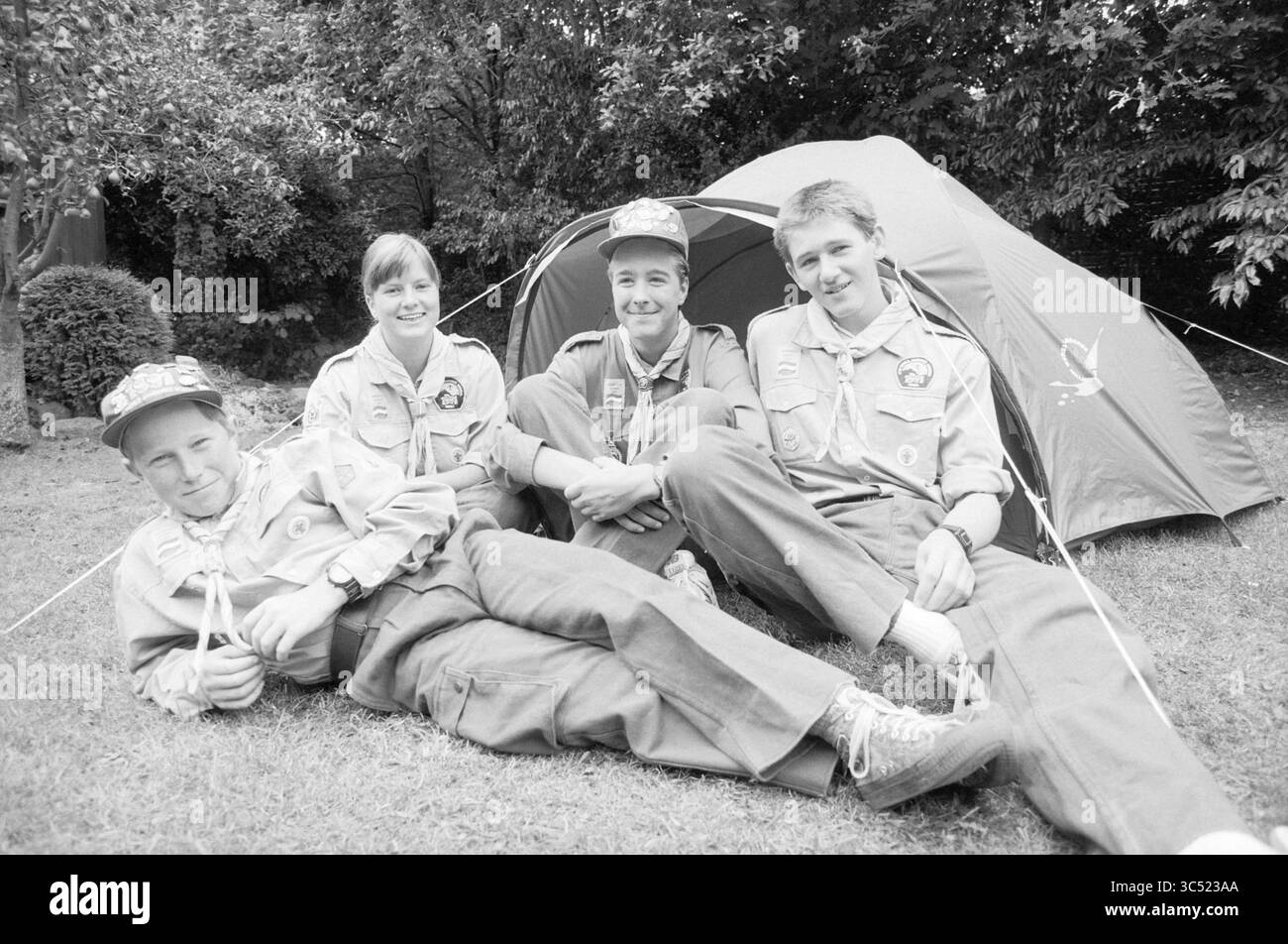 Four members scouting, Santpoort, Santpoort, 06-09-1991 Whizgle News, Dutch Desk, i Paesi Bassi, 1950-2000 quattro giovani esploratori si rilassano all'esterno di una tenda da campeggio, vestita con uniformi da scout e cappelli. Sono seduti sull'erba con sorrisi, mostrando cameratismo e spirito di avventura. Lo sfondo presenta alberi e un giardino ben tenuto. Foto Stock