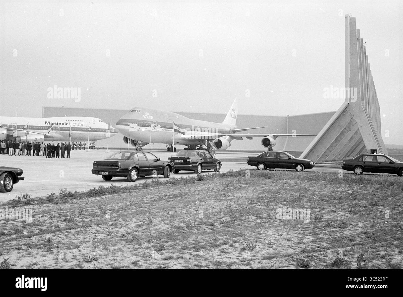 Barriera antirumore, Schiphol East, Schiphol, 30-06-1993 Whizgle News, Dutch Desk, i Paesi Bassi, 1950-2000 Un raduno di persone osserva due grandi aerei accanto a una fila di auto parcheggiate, con uno sfondo architettonico moderno in lontananza. La scena cattura un momento di storia dell'aviazione, mettendo in risalto sia gli aerei che i loro dintorni. Foto Stock