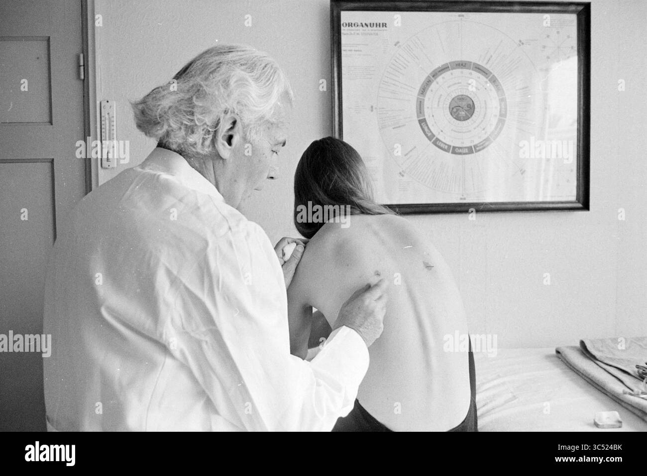 Il dottor Van der Waarden tratta un paziente con agopuntura, 24-11-1971 Whizgle News, Dutch Desk, Paesi Bassi, 1950-2000 Un professionista medico esamina la schiena di un paziente, concentrandosi su un'area specifica, mentre i grafici educativi sono visibili in background, suggerendo un ambiente clinico. Foto Stock