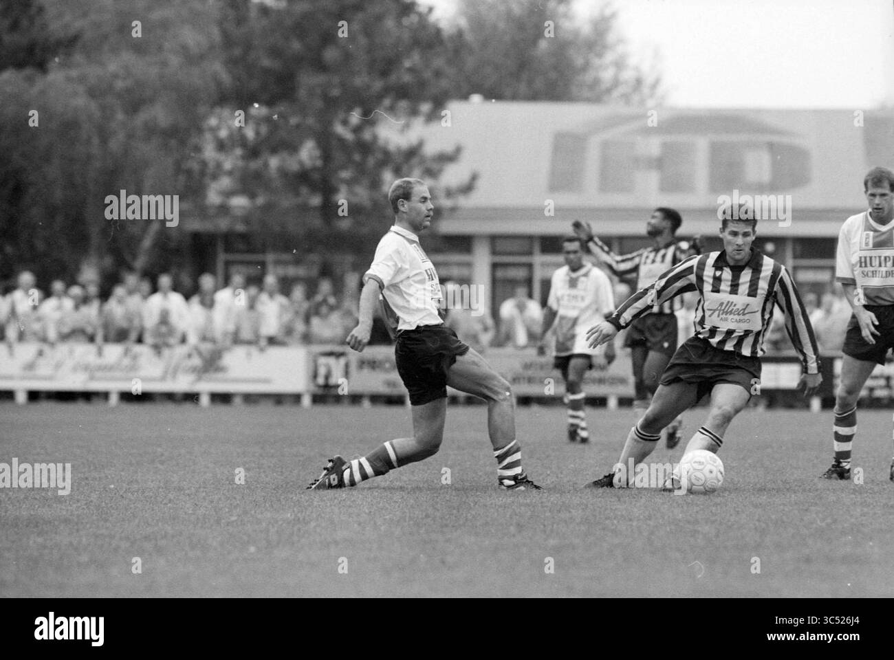 V.V.H. Velsen-Noord, Velsen-Noord, 01-09-1990 Whizgle News, Dutch Desk, Paesi Bassi, 1950-2000 due giocatori di calcio sono impegnati in un gioco competitivo sul campo, uno tenta di affrontare la palla mentre l'altro manovra abilmente per mantenere il possesso. Una folla può essere vista sullo sfondo, concentrata sull'azione. Foto Stock