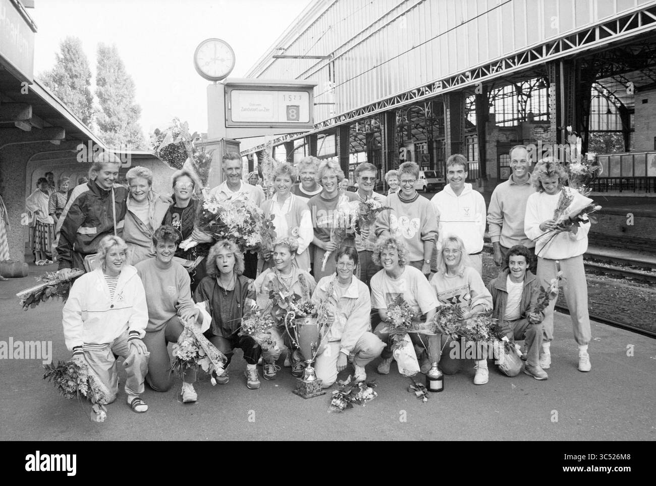 Arrivo terrazza Birds softball station Haarlem, Softball, Haarlem, Paesi Bassi, 25-09-1989 Whizgle News, Dutch Desk, Paesi Bassi, 1950-2000 Un gruppo gioioso di atleti e tifosi festeggia insieme in una stazione ferroviaria, tenendo fiori e trofei, sorridendo tutto intorno mentre commemorano un evento di successo. Un orologio sullo sfondo segna l'ora, aggiungendo un senso di occasione memorabile. Foto Stock