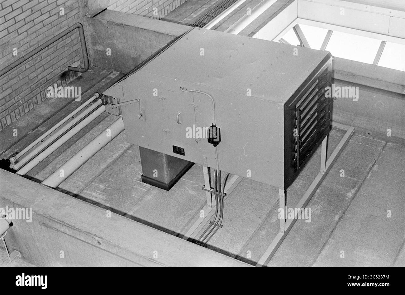 Centrale elettrica alimentata a petrolio N.Z.H. garage di Haarlem, Noord Zuid Hollandse Vervoersmaatschappij N.V., NZ, Heating, Haarlem, Leidsevaart, paesi Bassi, 05-09-1961 Whizgle News, Dutch Desk, Paesi Bassi, 1950-2000 Una grande unità di climatizzazione industriale è montata sopra, circondata da condotti e tubi esposti. L'ambiente presenta pareti in cemento, suggerendo un design utilitario. La luce naturale filtra attraverso le alte finestre, illuminando l'area. Foto Stock