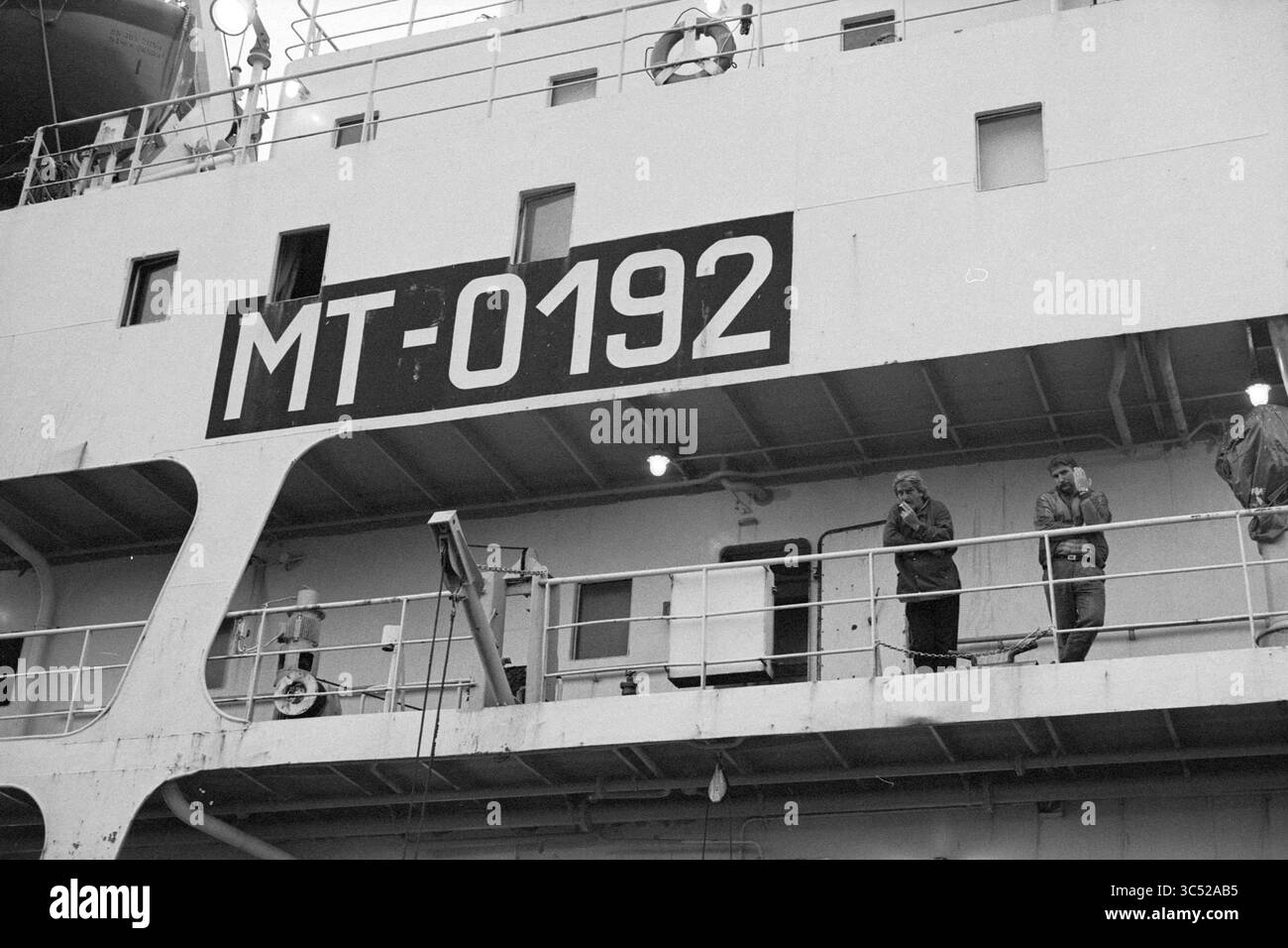 Dettaglio di una nave proveniente da Malta Whizgle News, Dutch Desk, Paesi Bassi, 1950-2000 due persone si trovano sul ponte di una nave, con un grande numero di identificazione, MT-0192, ben visibile. L'ambientazione suggerisce un ambiente di lavoro, con varie strutture e ringhiere tipiche di una nave. Foto Stock