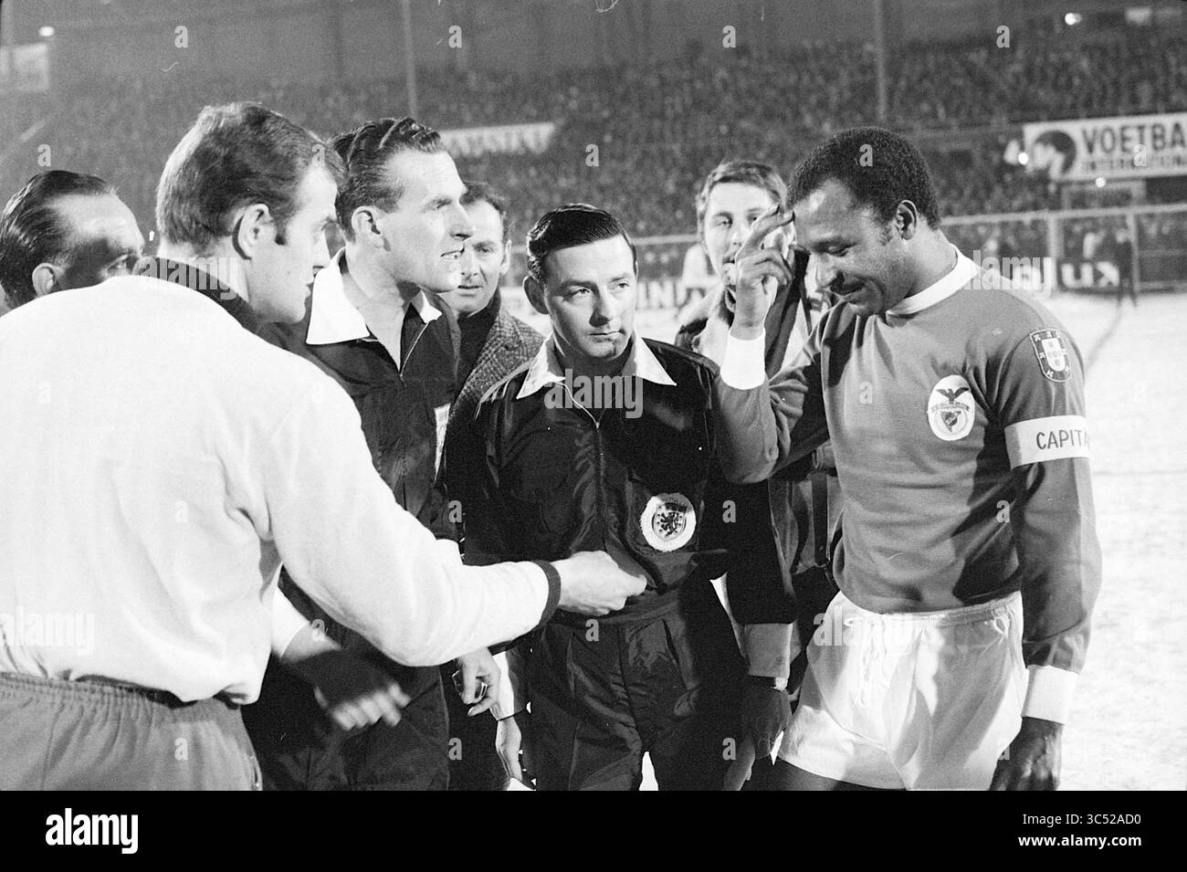 AJAX - Benfica, Football Ajax, 12-02-1969 Whizgle News, Dutch Desk, Paesi Bassi, 1950-2000 Un gruppo di giocatori e funzionari si riunisce sul campo per una stretta di mano pre-partita, mostrando cameratismo e sportività prima dell'inizio della partita. L'attenzione è rivolta a un capitano con una maglia rossa, evidenziata mentre si impegna con l'arbitro. Foto Stock