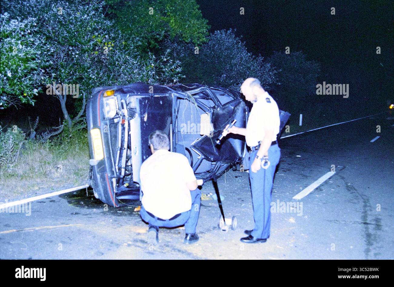Incidente, Zeeweg, 21-08-1995 Whizgle News, Dutch Desk, Paesi Bassi, 1950-2000 due persone stanno ispezionando un veicolo rovesciato sul lato di una strada, circondato da alberi. La scena suggerisce un recente incidente, con i soccorritori che esaminano da vicino la situazione. Foto Stock