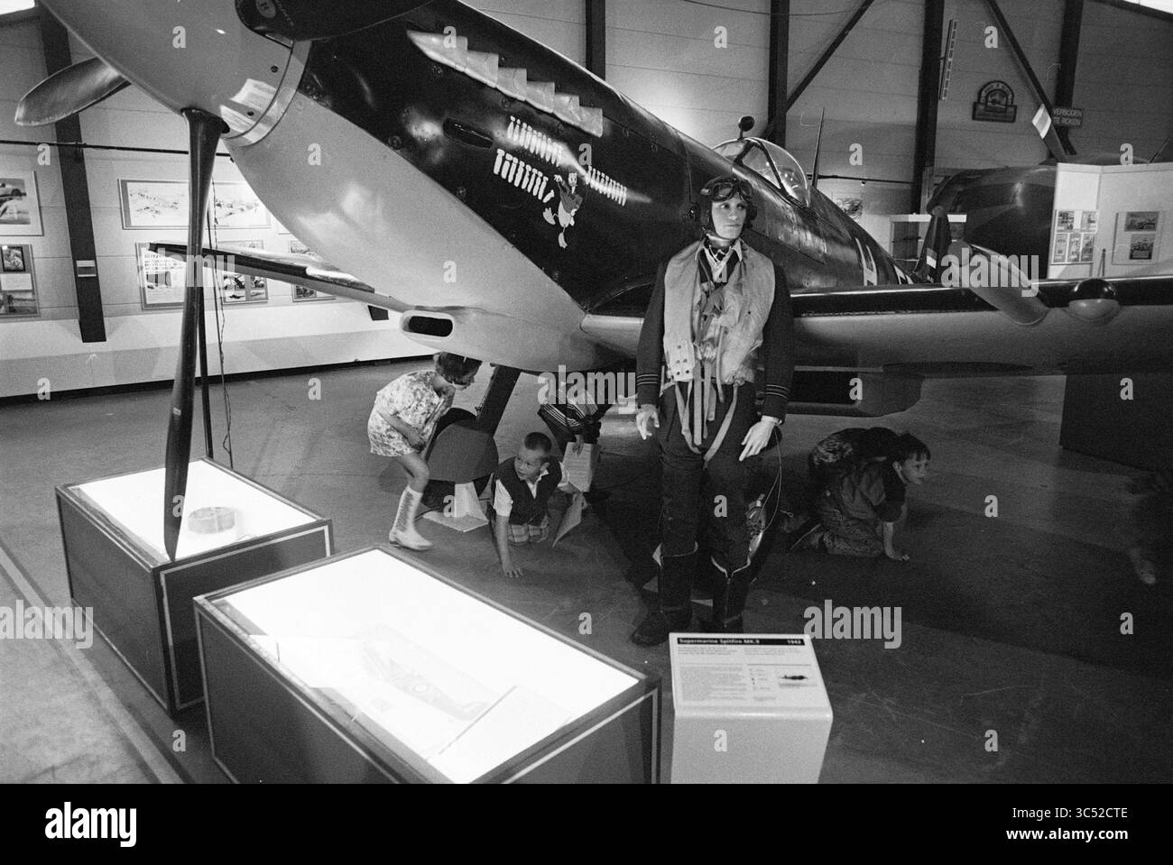 Aviodome, Spitfire, 17-05-1994 Whizgle News, Dutch Desk, Paesi Bassi, 1950-2000 Un velivolo storico è al centro della scena in un museo, accompagnato da una figura a grandezza naturale di un pilota vestito con equipaggiamento d'epoca. In primo piano, i bambini esplorano le mostre, affascinati dalle mostre sulla storia dell'aviazione intorno a loro. Foto Stock