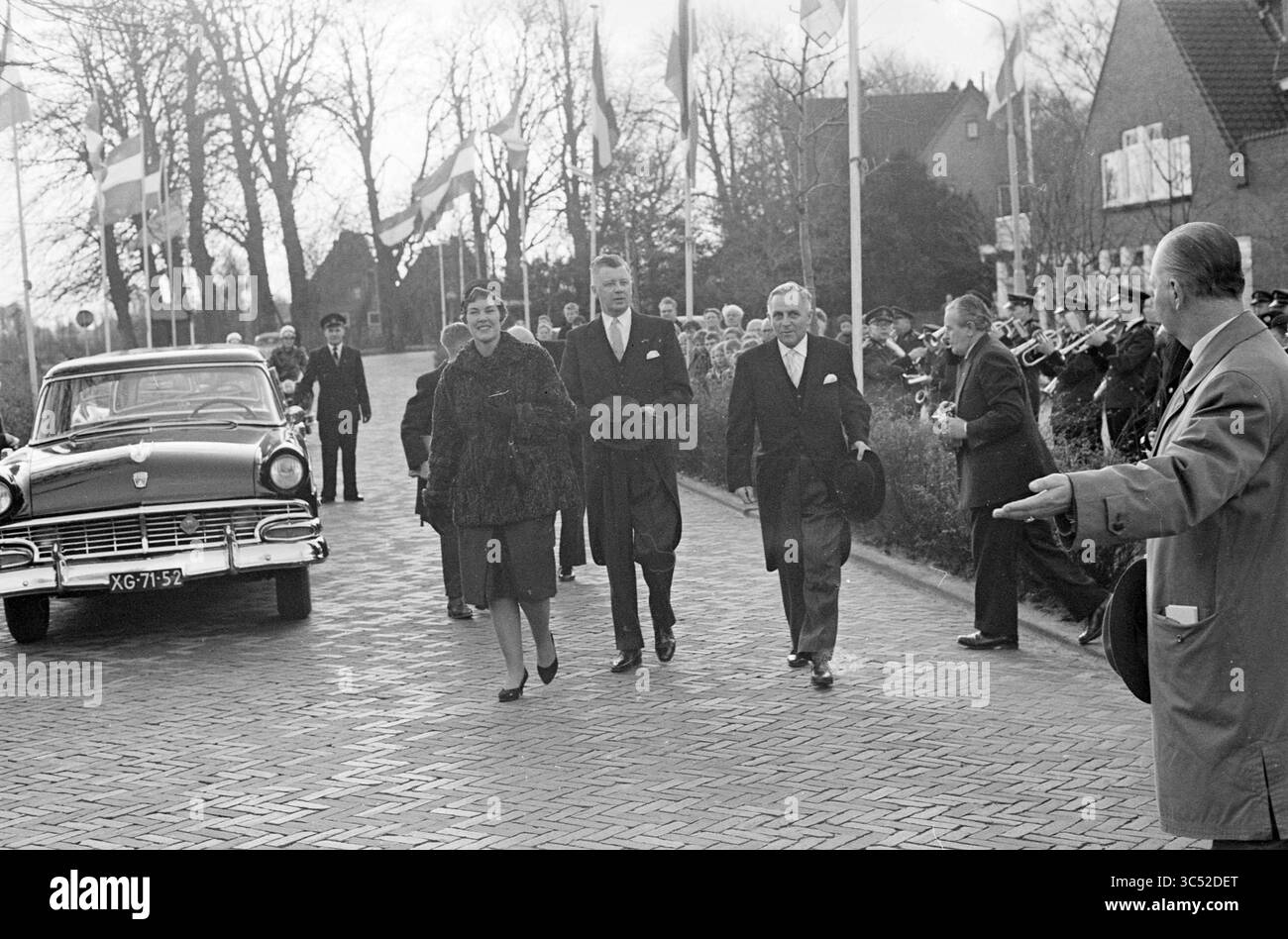 Insediamento del sindaco Buhrmann Velsen, Mayors, IJmuiden, Velsen, 02-12-1960 Whizgle News, Dutch Desk, Paesi Bassi, 1950-2000 Una processione formale con un gruppo di dignitari che camminano lungo un sentiero lastricato, fiancheggiato da bandiere e un pubblico. L'atmosfera è festosa, con una band che suona in sottofondo mentre si avvicinano a un'auto d'epoca. Foto Stock