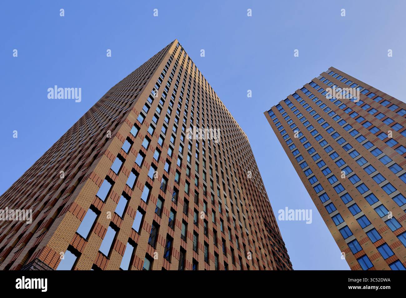 Le torri gemelle in mattoni di Amsterdam si innalzano su un cielo azzurro e mostrano finestre ripetute e motivi geometrici, incarnando un audace design urbano moderno. Foto Stock