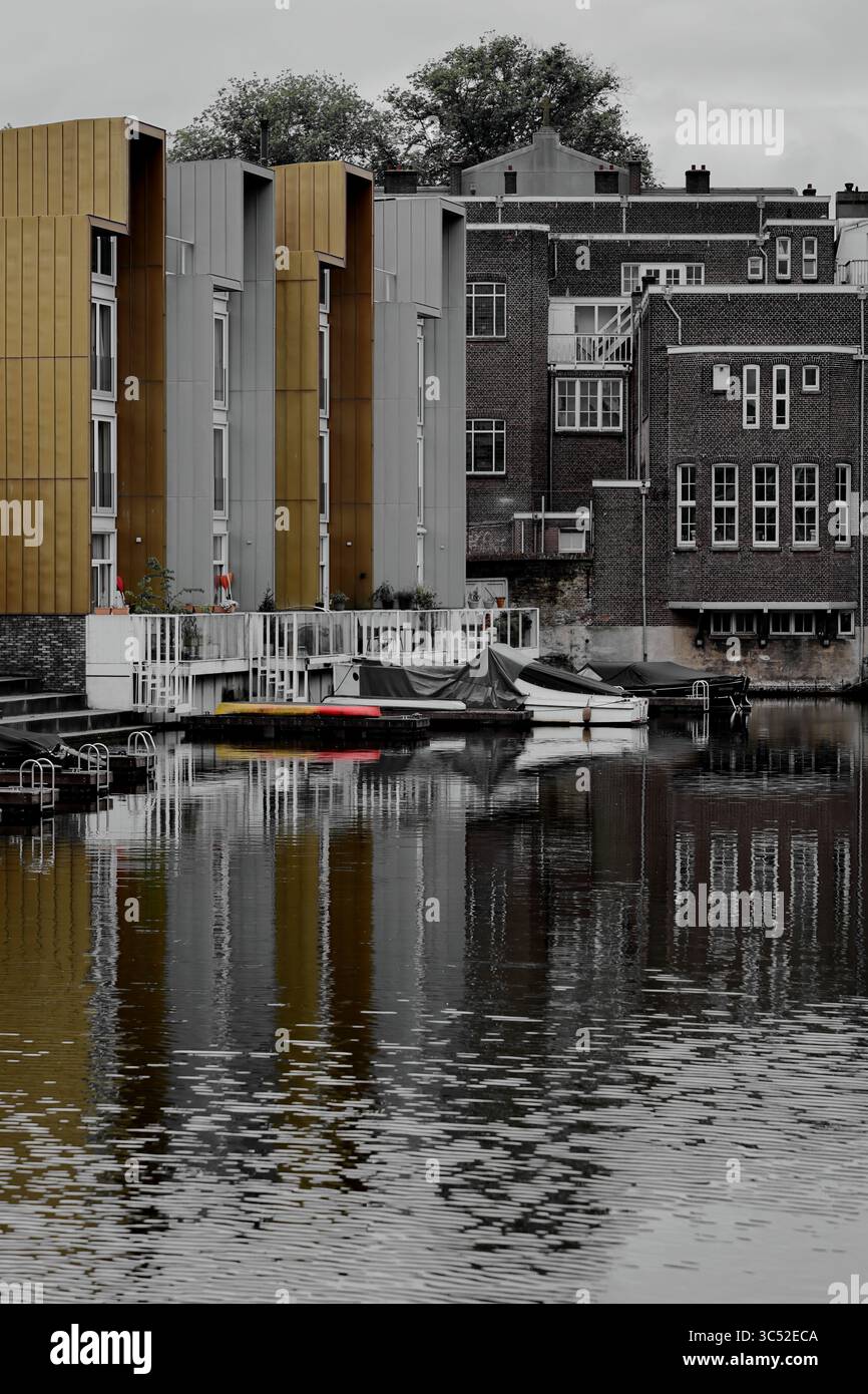 La vista monocromatica dal Ponte Ezelsbrug di Amsterdam contrasta una facciata dorata con un edificio in mattoni che si riflette nell'acqua, creando una scena lunare. Foto Stock