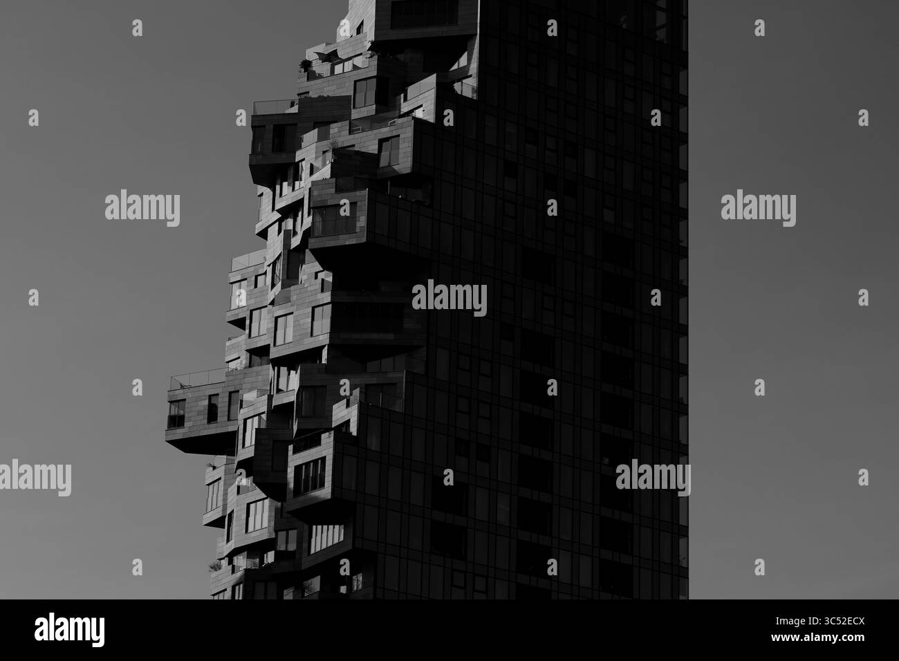 La cattura monocromatica di una torre della Valle di Amsterdam mette in evidenza terrazze frastagliate e facciata ombreggiata contro il cielo moodico, enfatizzando l'architettura moderna. Foto Stock