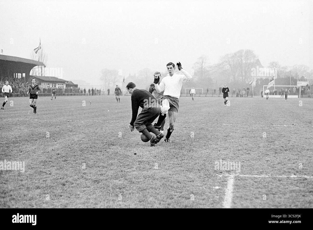 H.F.C. - A.F.C., calcio, 12-01-1964 Whizgle News, Dutch Desk, Paesi Bassi, 1950-2000 Una partita di calcio si svolge su un campo nebbioso, dove i giocatori delle squadre avversarie si impegnano in un gioco dinamico. Un giocatore manovra abilmente la palla, mentre un altro tenta di difendersi. Gli spettatori sullo sfondo guardano attentamente, circondati dall'atmosfera vivace del gioco. Foto Stock