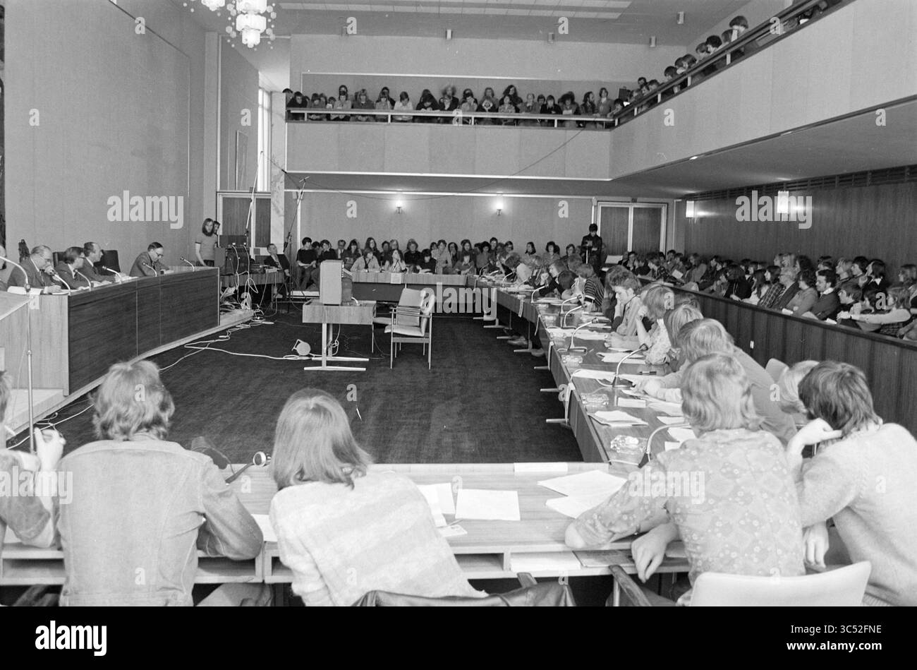 Frazioni scolastiche in Velsen Municipal Council, Velsen Municipal Council, Schools, 08-04-1976 Whizgle News, Dutch Desk, i Paesi Bassi, 1950-2000 Un grande raduno in una sala conferenze, con un pannello di relatori davanti e un pubblico seduto in fila. L'ambiente è caratterizzato da lunghi tavoli e sedie, con i partecipanti che ascoltano e prendono appunti con attenzione, creando un'atmosfera di discussione e di coinvolgimento. Foto Stock