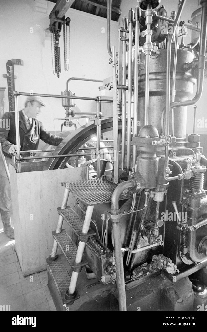 Stazione di pompaggio Velserbroek, stazione di pompaggio a vapore e stazione di pompaggio a vapore, 15-04-1976 Whizgle News, Dutch Desk, Paesi Bassi, 1950-2000 Un motore a vapore d'epoca con macchinari e tubazioni intricati, accanto a un lavoratore esperto che regola il meccanismo, riflettendo un periodo di innovazione industriale. Foto Stock