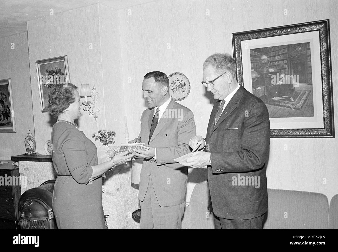 La sig.ra Auben dà 10 Grand, persone, 17-11-1965 Whizgle News, Dutch Desk, Paesi Bassi, 1950-2000 Una donna presenta un rotolo o un certificato ad un uomo, mentre un altro uomo sta accanto a loro, osservando entrambi lo scambio con interesse. L'ambiente presenta pareti decorative e un ambiente interno accogliente. Foto Stock