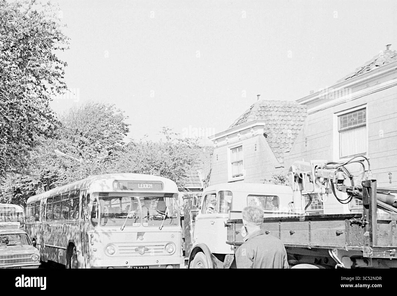 Bambini con autobus, Duinrell, bambini, bambini, case per bambini, festa per bambini, bambini, 21-07-1967 Whizgle News, Dutch Desk, Paesi Bassi, 1950-2000 Una vivace scena stradale con un autobus d'epoca che mostra la destinazione "Leiden", oltre a diverse auto parcheggiate e un camion. Gli alberi fiancheggiano la strada e le case vicine mostrano un'architettura tradizionale. Una persona si trova vicino alla strada, osservando l'attività. Foto Stock