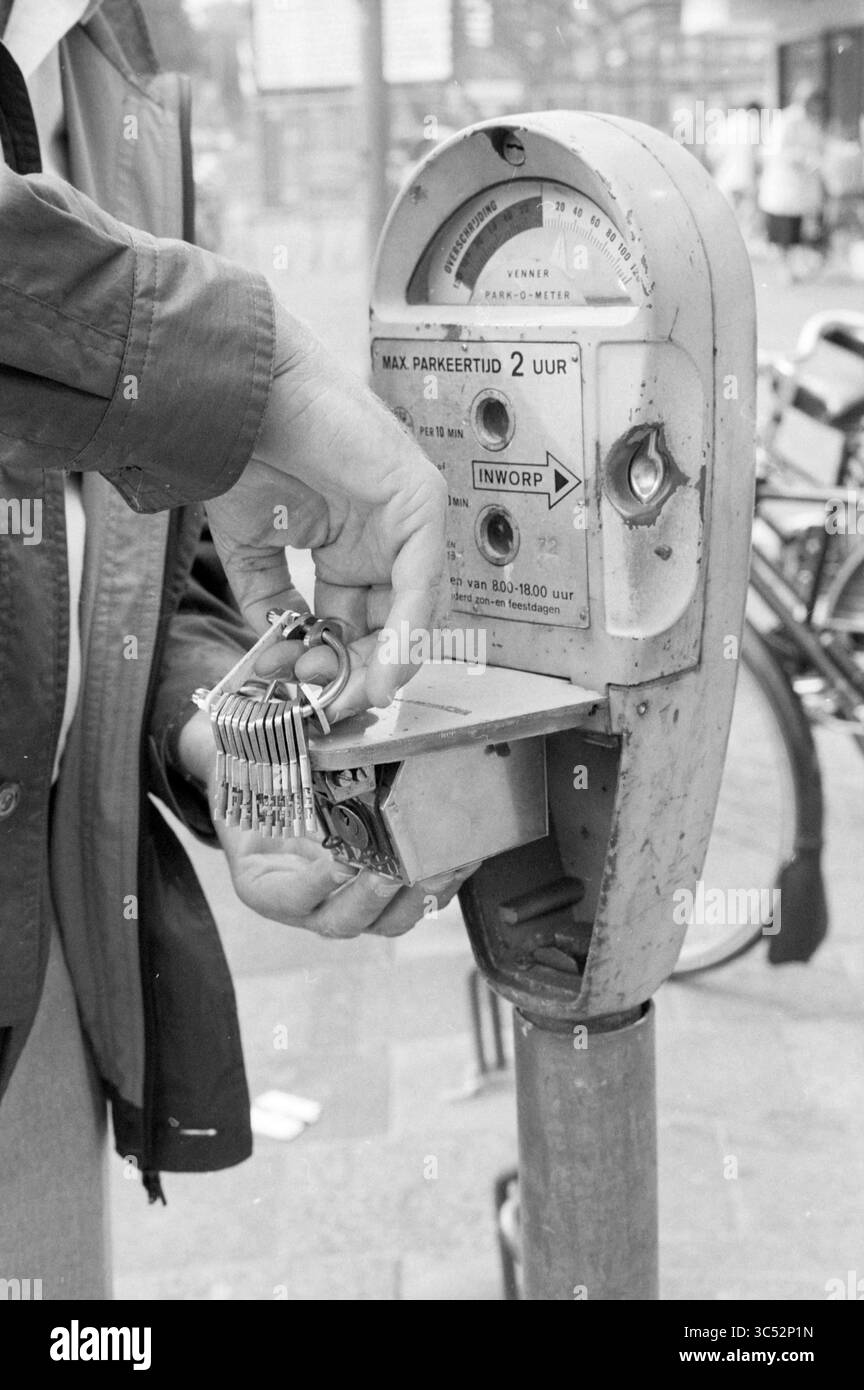 The attribute + Solutions parking attendant Nico sprang, Parking, Parking, Parking lots, Parking lots, 12-09-1989 Whizgle News, Dutch Desk, Paesi Bassi, 1950-2000 Una mano tiene una serie di chiavi vicino a un vecchio parchimetro, poiché le monete sono inserite per pagare il parcheggio. Lo sfondo presenta biciclette e pedoni, che fanno pensare a un ambiente urbano frenetico. Foto Stock