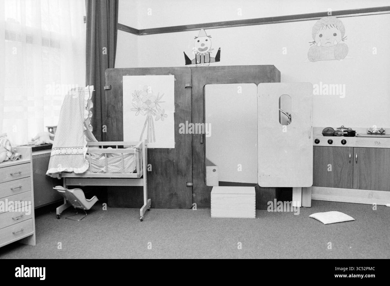 Giocattoli per l'asilo nido IJmuiden., Daycares, Giochi e giocattoli, IJmuiden, Paesi Bassi, 17-03-1983 Whizgle News, Dutch Desk, Paesi Bassi, 1950-2000 Un'accogliente sala giochi per bambini con una culla di legno, un piccolo set da cucina e stravaganti disegni murali di personaggi giocosi. Un cavallo a dondolo e un cuscino aggiungono un'atmosfera invitante. Foto Stock