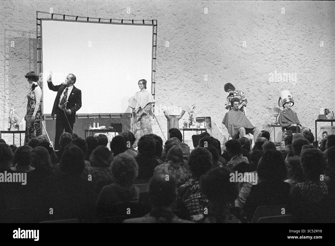 Dimostrazione di parrucchiere a Schalkererf, dimostrazione, parrucchieri e parrucchieri, Haarlem, Bernadottelaan, Paesi Bassi, 24-02-1975 Whizgle News, Dutch Desk, Paesi Bassi, 1950-2000 Una vivace presentazione sul palco presenta un altoparlante ben vestito che coinvolge il pubblico, mentre i modelli mostrano acconciature eleganti, con parrucchieri pronti all'azione. Elementi decorativi e un grande schermo contribuiscono a creare l'atmosfera di un evento dimostrativo di bellezza. Foto Stock