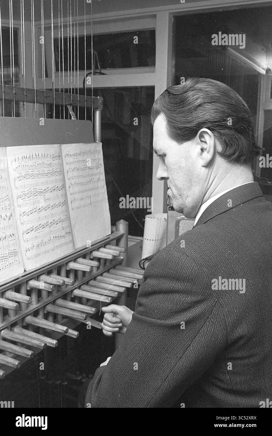 Carillonneur Han de Ligt, musica, persone, 11-12-1967 Whizgle News, Dutch Desk, paesi Bassi, 1950-2000 Un uomo lavora intensamente su un grande dispositivo meccanico, regolando le impostazioni mentre studia un foglio di musica stampata. L'intricato macchinario mostra una serie di aste o leve metalliche, che riflettono l'attenzione sull'intersezione tra musica e tecnologia. Foto Stock