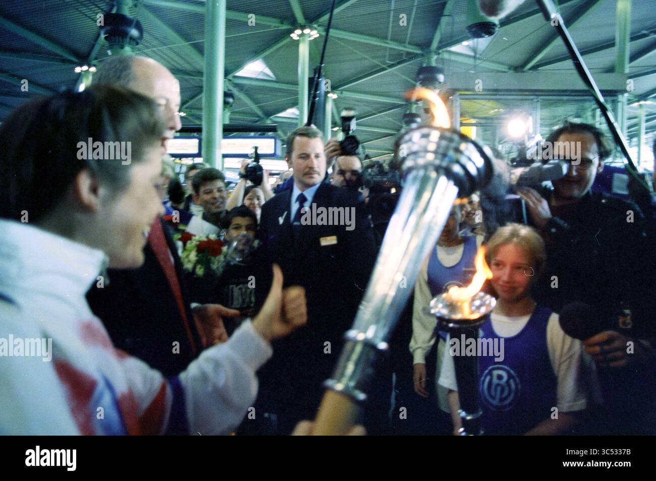 Arrivo della fiamma olimpica, Schiphol, Schiphol, 06-04-1996 Whizgle News, Dutch Desk, i Paesi Bassi, 1950-2000 Un gruppo di spettatori entusiasti si riunisce mentre un giovane atleta tiene con orgoglio una torcia accesa con le fiamme, simboleggiando un evento significativo. Tra la folla, una figura in una tuta osserva con attenzione, mentre altri partecipanti mostrano espressioni di gioia e anticipazione. L'atmosfera e' vivace, piena del trambusto di un'occasione memorabile. Foto Stock