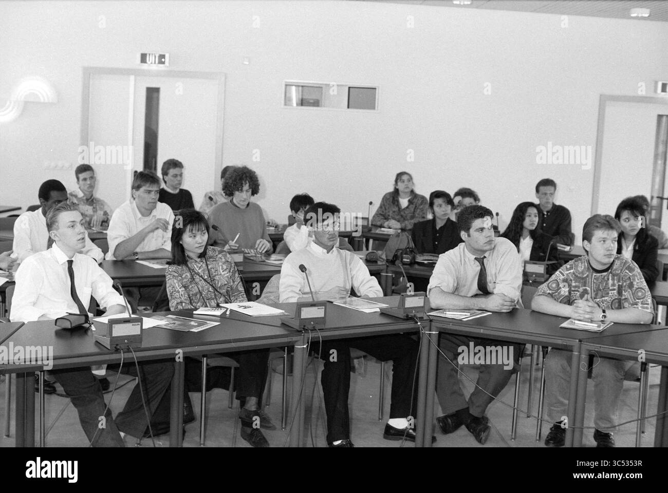 Studenti di inglese presso la camera di commercio di Haarlem, Paesi Bassi, 14-04-1991 Whizgle News, Dutch Desk, i Paesi Bassi, 1950-2000 Un gruppo eterogeneo di studenti ascolta attentamente durante una lezione in aula, seduti a tavoli dotati di microfoni e appunti davanti a loro. Foto Stock