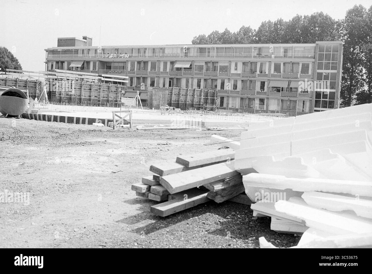 Nuova costruzione a casa di riposo Meerstede Hoofddorp, nuova costruzione, Hoofddorp, Paesi Bassi, 26-06-1989 Whizgle News, Dutch Desk, Paesi Bassi, 1950-2000 Un cantiere presenta un edificio a più piani in corso, circondato da pile di legname e materiali da costruzione. In primo piano, i fogli di isolamento sono impilati, mentre l'edificio mostra segni di lavori incompleti, con impalcature visibili. Gli alberi allineano lo sfondo, aggiungendo un tocco di natura alla scena industriale. Foto Stock