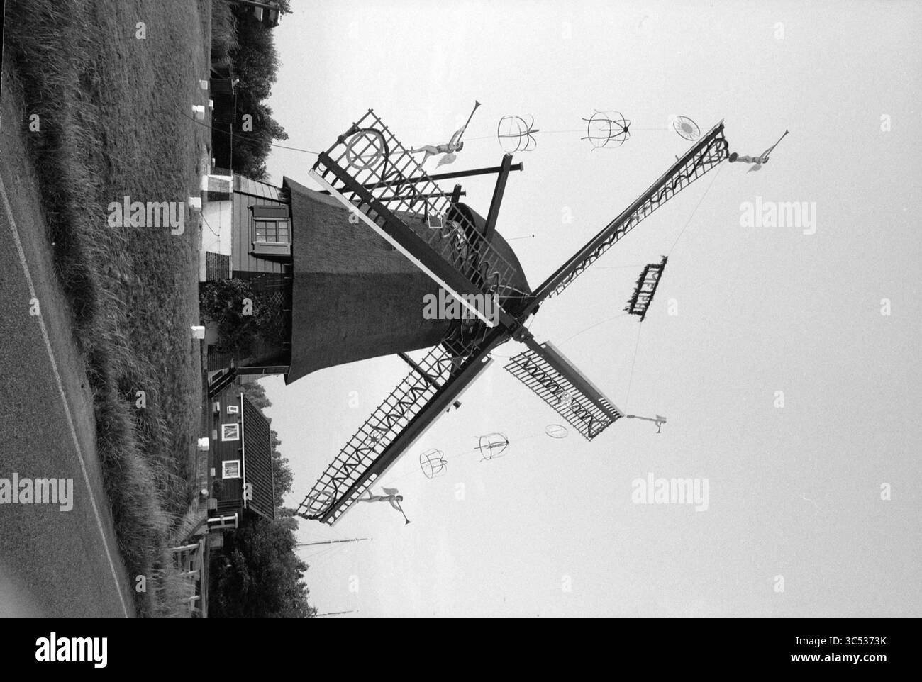 Mulino a vento decorato con estensione De Veer, 09-08-1991 Whizgle News, Dutch Desk, Paesi Bassi, 1950-2000 Un mulino a vento tradizionale si erge in rilievo contro un cielo limpido, con le sue vele allungate e rivolte verso il vento. La struttura è circondata da vegetazione lussureggiante e una strada conduce alla base del mulino a vento, esaltandone il fascino rustico. Foto Stock
